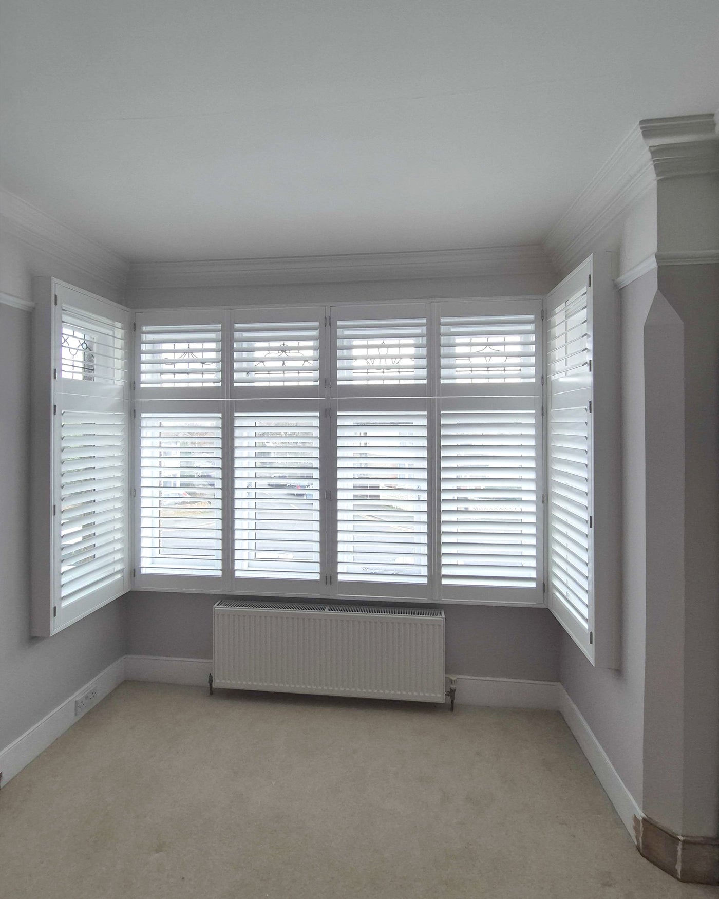 Full height shutters on a period-style bay window with stained-glass detail